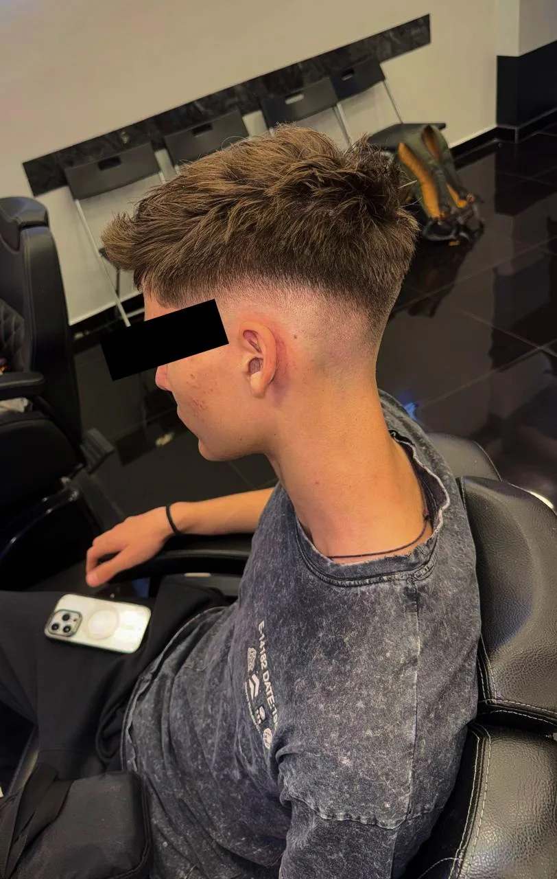 Client pe scaunul de frizerie cu o tunsoare texturată și fade, vedere laterală