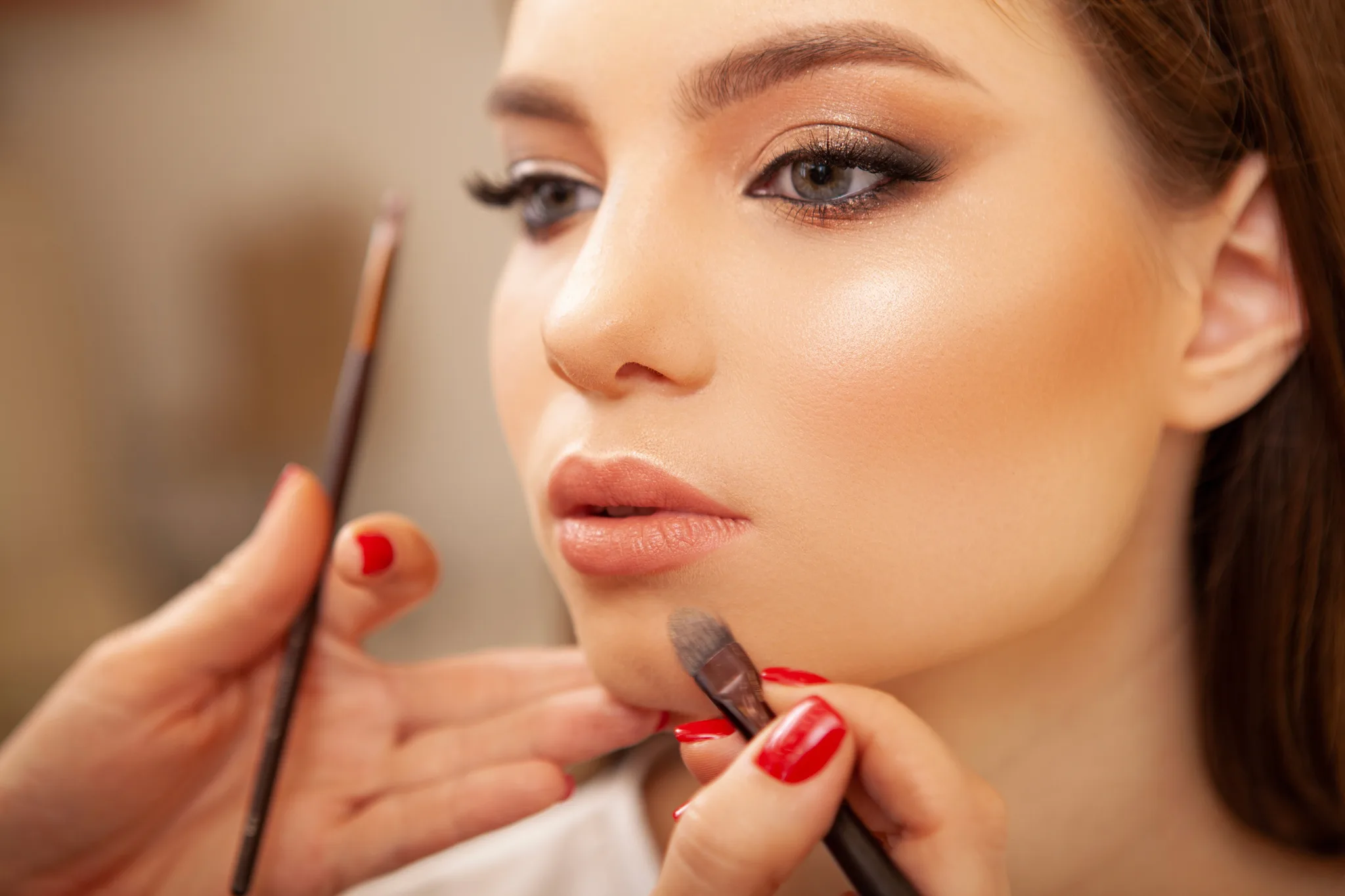 Make-up artist aplică ruj cu pensula pe buzele unei cliente, machiaj natural de zi
