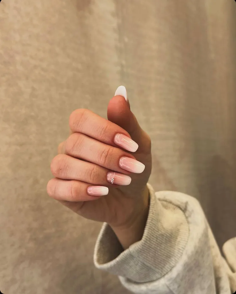 Manichiură baby boomer, din nude spre alb, cu un mic model pe inelar
